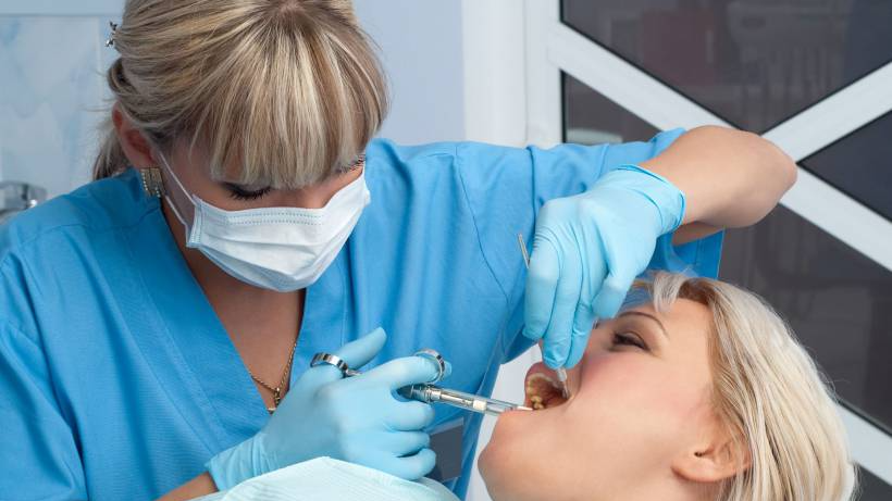Anestesia dentária: tudo que você precisa saber. Dentista de máscara realizando procedimento em paciente feminina.