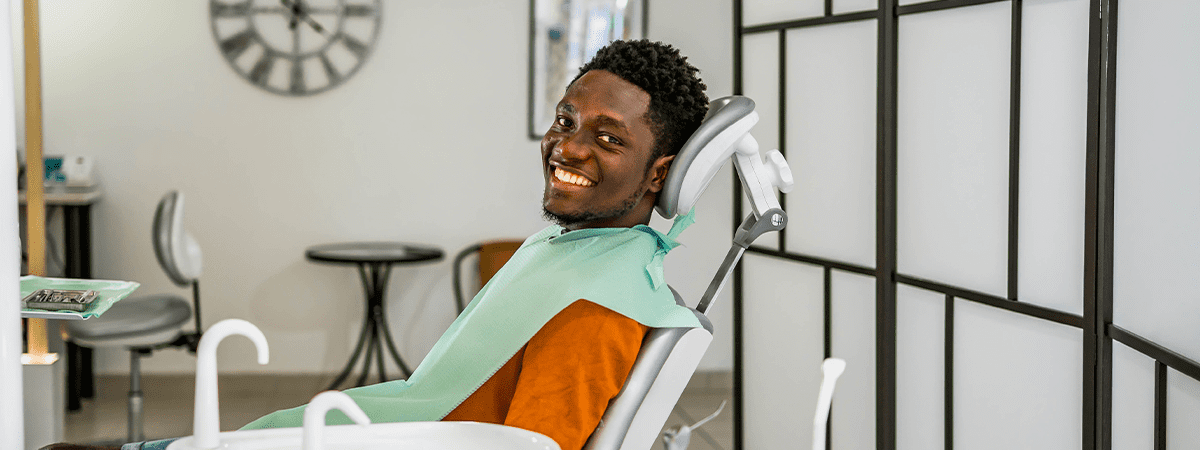 Homem negro sorridente sentado na cadeira de dentista aguardando o tratamento de canal no dente