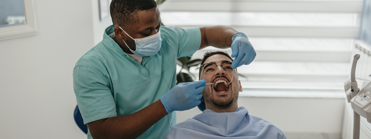  Dentista utilizando instrumentos para examinar a boca de um paciente sentado na cadeira odontológica.