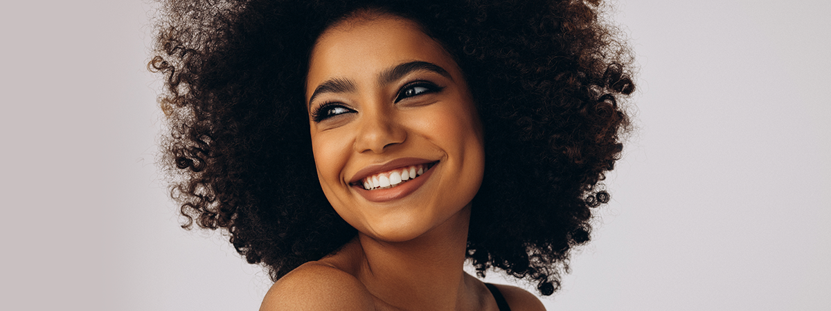 Mulher sorridente com cabelo afro volumoso em fundo neutro. 