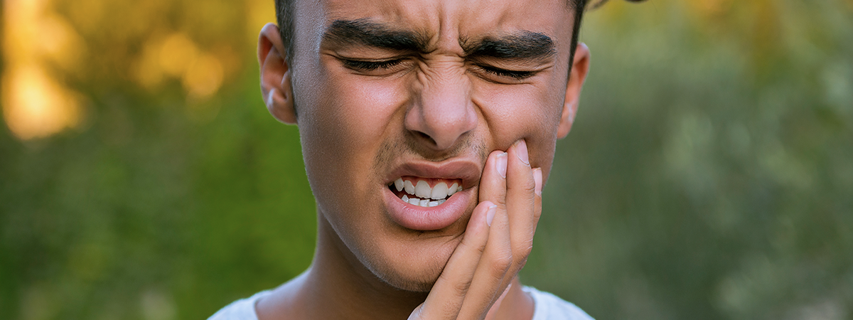  homem jovem expressando dor de dente ao segurar a bochecha