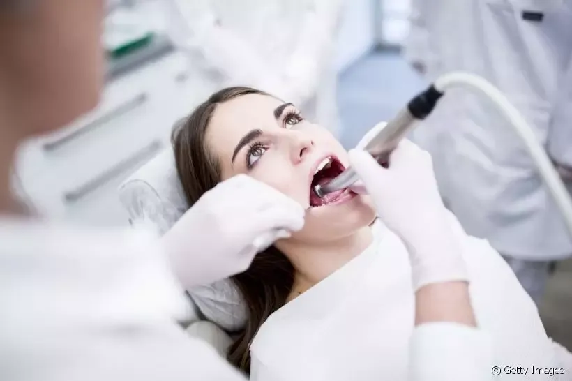 Mulher jovem recebendo tratamento dentário extraçao do siso, enquanto um dentista com luvas realiza procedimentos em sua boca. 