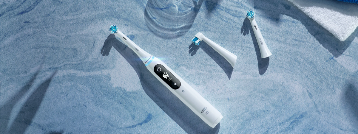 Escova de dente elétrica branca com cabeças substituíveis sobre uma superfície azulada.