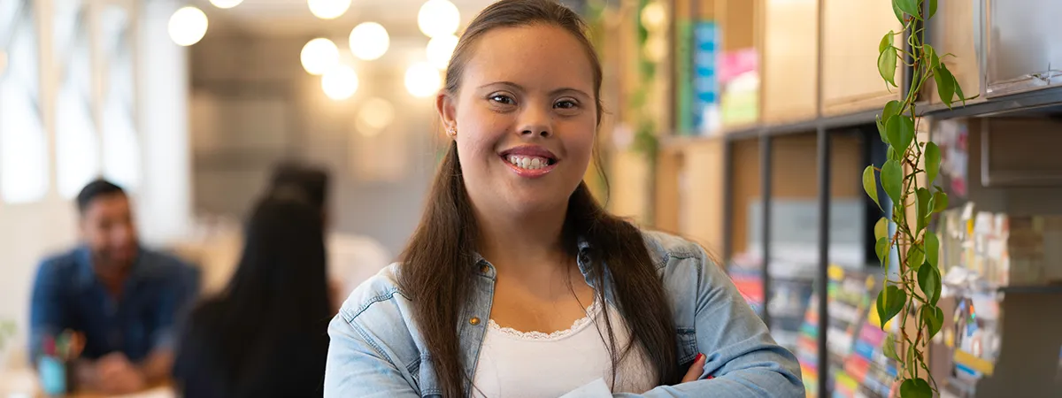 Mulher jovem com síndrome de Down sorrindo para a câmera em um ambiente de escritório iluminado.