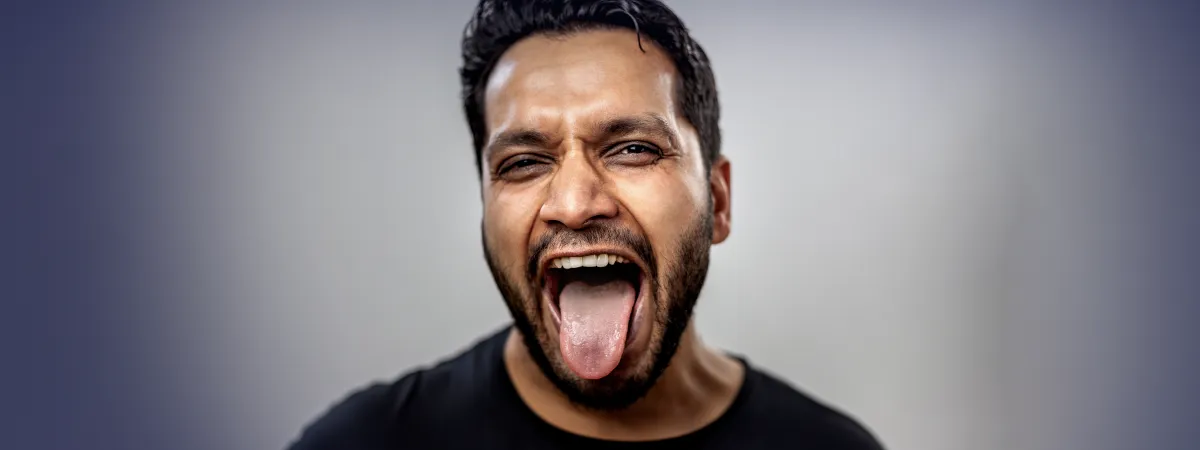 Homem com expressão intensa mostrando a língua para fora, representando sensações de sabores ruins na boca.