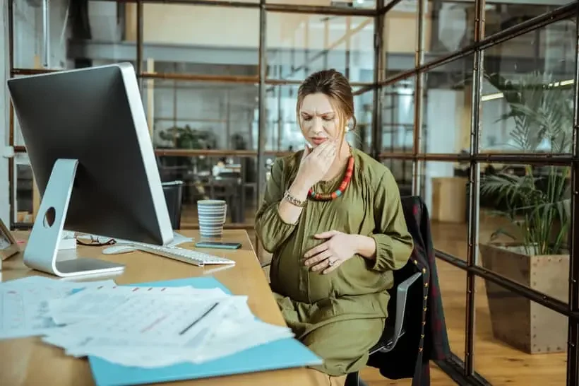 Mulher grávida sentada em sua mesa no escritório, parecendo desconfortável com dor de dente