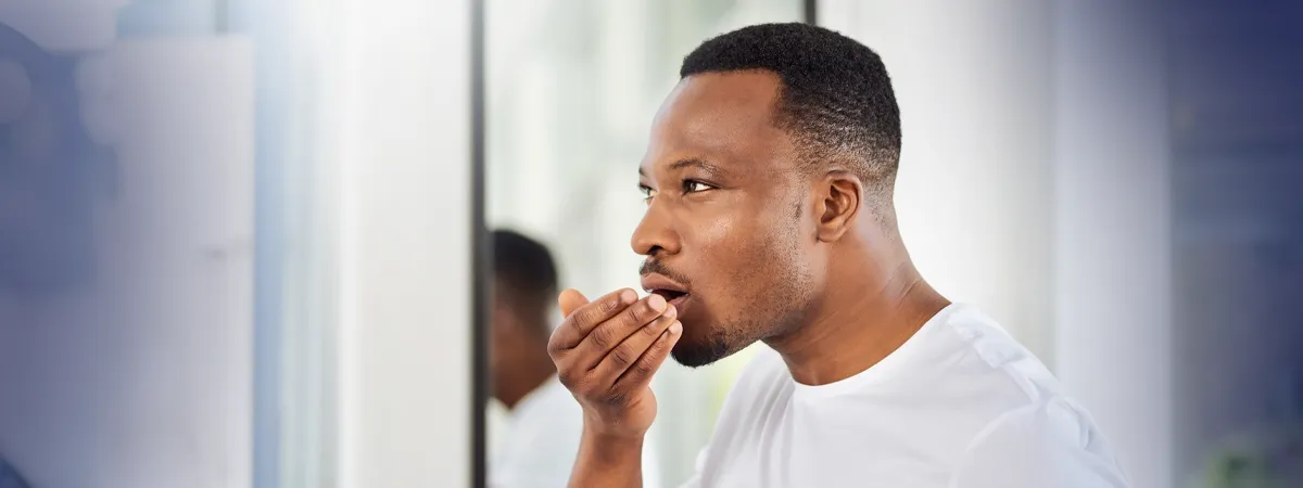 Homem negro de camiseta branca examinando seu hálito, ilustrando preocupações com saúde bucal e mau hálito