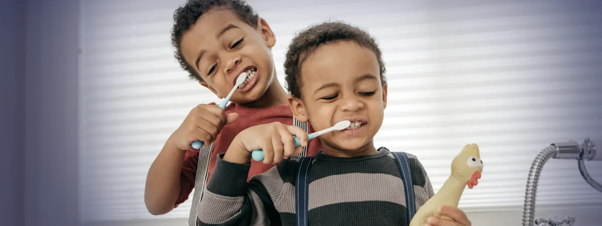 Dois irmãos brincando de escovar os dentes, destacando a importância da saúde bucal infantil