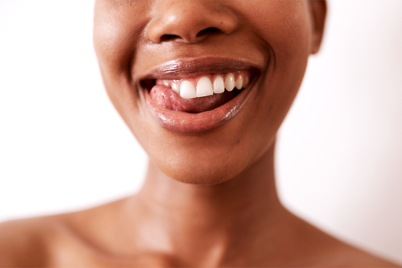 Sorriso de mulher jovem com pele negra, mostrando dentes, com fundo neutro